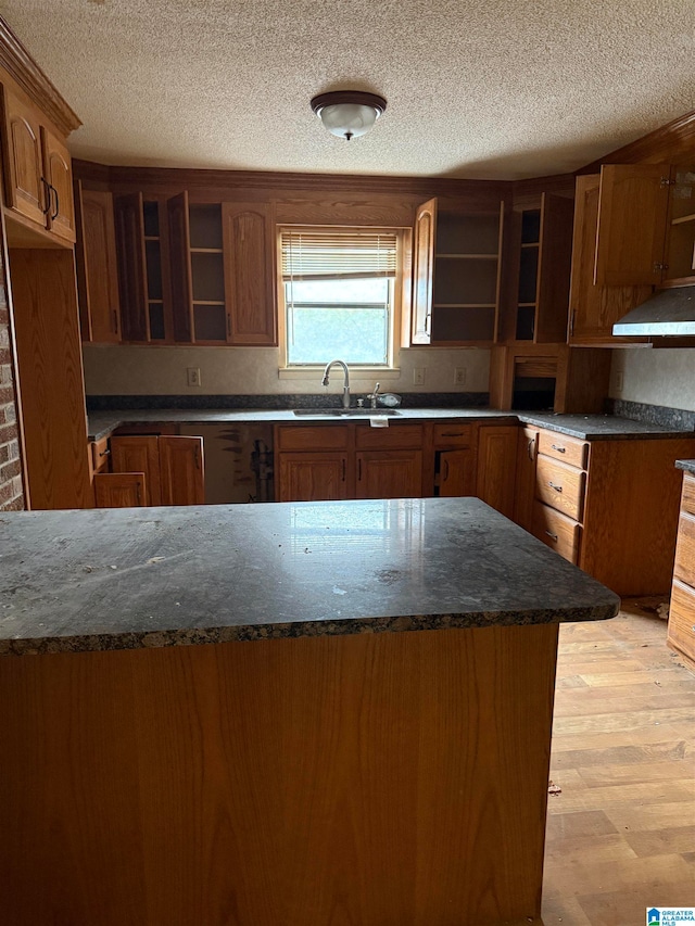 kitchen with dark stone counters, sink, light wood-type flooring, and a textured ceiling