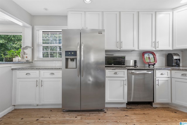 kitchen with light wood-type flooring, appliances with stainless steel finishes, white cabinets, and tasteful backsplash