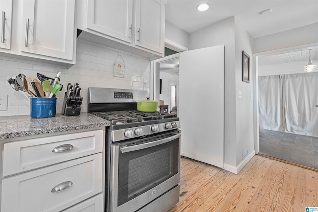 kitchen featuring gas range, light stone countertops, backsplash, light wood-type flooring, and white cabinets