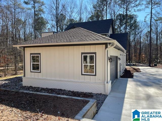 view of side of property featuring board and batten siding, an attached garage, driveway, and roof with shingles