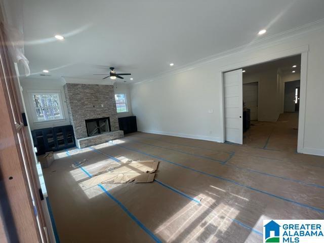 unfurnished living room featuring crown molding, baseboards, a ceiling fan, and a stone fireplace