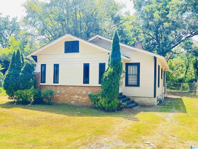 view of side of property featuring brick siding, a yard, a chimney, and fence