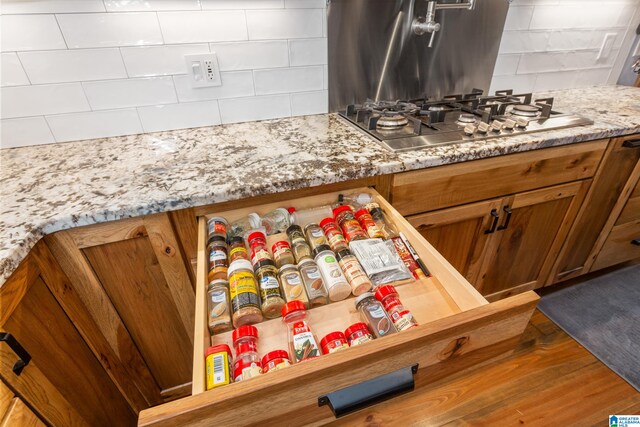 room details featuring stainless steel gas cooktop, light stone counters, and wood-type flooring