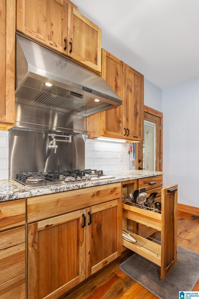 kitchen with stainless steel gas stovetop, dark hardwood / wood-style floors, light stone countertops, and decorative backsplash