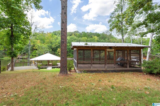 back of property with a water view, a lawn, and a sunroom