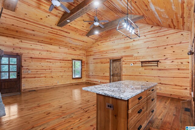 kitchen featuring a kitchen island, wood walls, hanging light fixtures, ceiling fan, and light stone counters