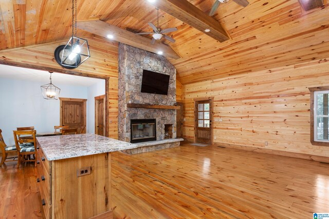 kitchen featuring light wood-type flooring, a fireplace, light stone counters, ceiling fan, and hanging light fixtures