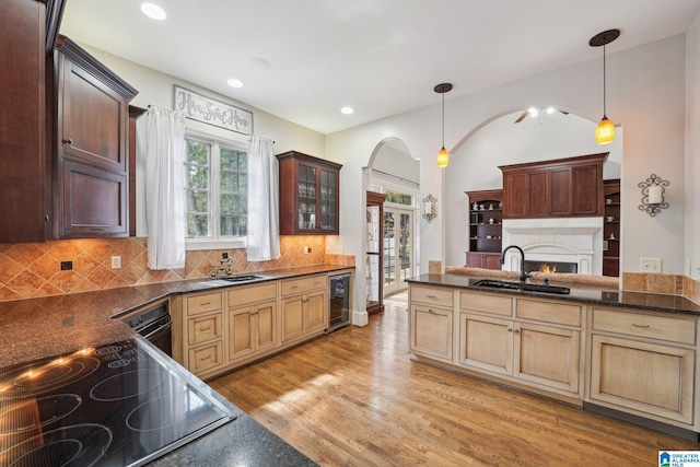 kitchen with wine cooler, light wood-type flooring, decorative light fixtures, cooktop, and sink