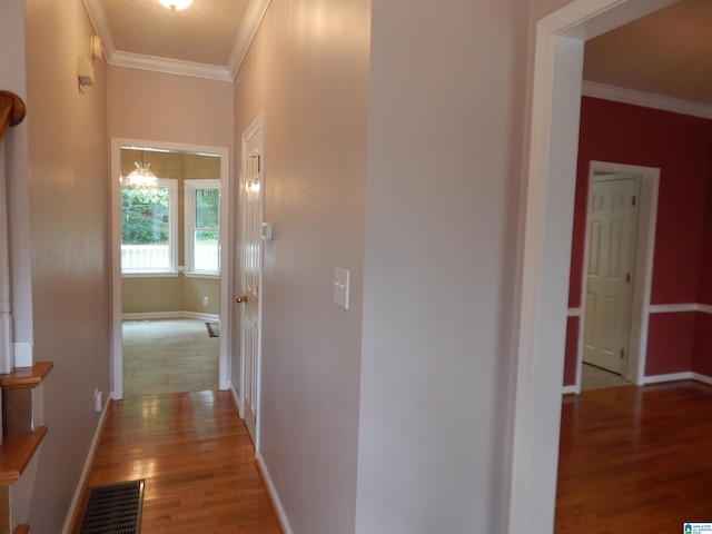 hall with light wood-type flooring, ornamental molding, and a chandelier