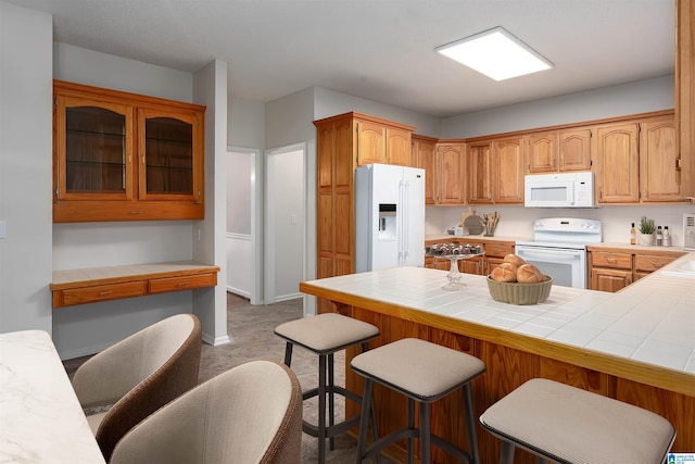 kitchen featuring a kitchen breakfast bar, tile countertops, kitchen peninsula, and white appliances