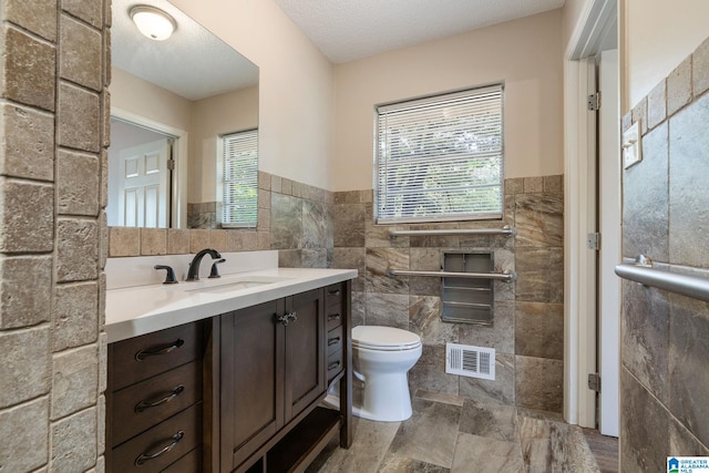 bathroom with vanity, tile walls, toilet, and a textured ceiling