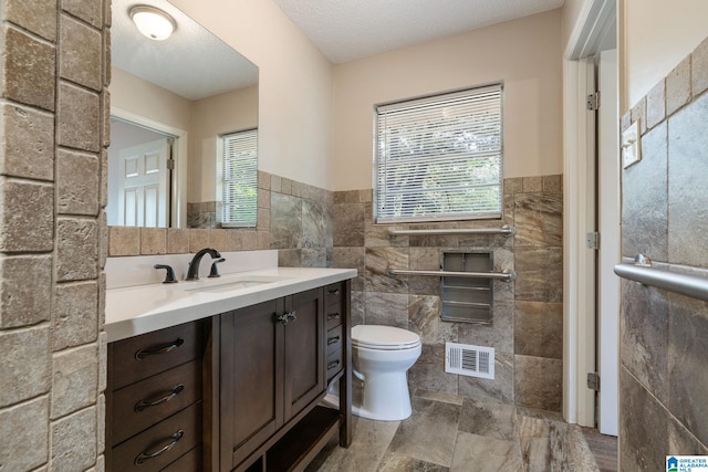 bathroom with toilet, vanity, tile walls, and visible vents