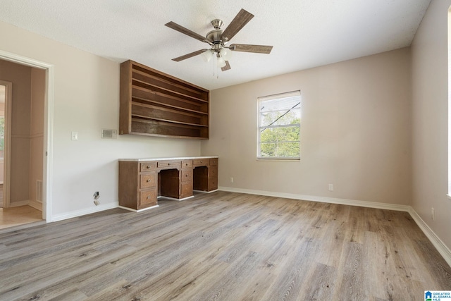 interior space featuring light wood-type flooring, built in desk, ceiling fan, and a textured ceiling