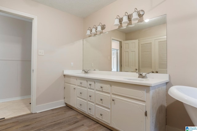 bathroom with baseboards, a textured ceiling, a sink, double vanity, and wood finished floors