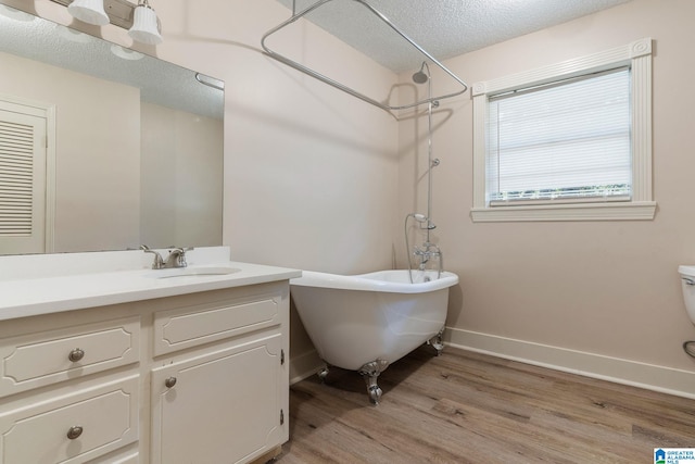 bathroom featuring vanity, wood finished floors, a textured ceiling, baseboards, and a freestanding bath