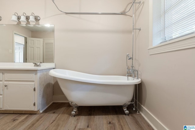 full bathroom with baseboards, wood finished floors, vanity, and a freestanding bath
