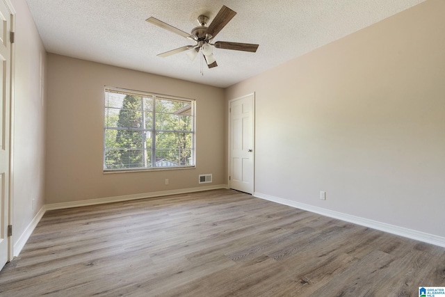 empty room with a ceiling fan, a textured ceiling, light wood-style flooring, baseboards, and visible vents