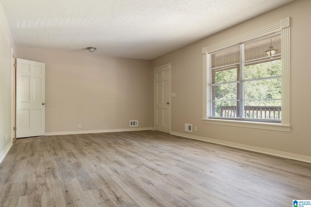 empty room featuring baseboards, a textured ceiling, visible vents, and light wood-style floors