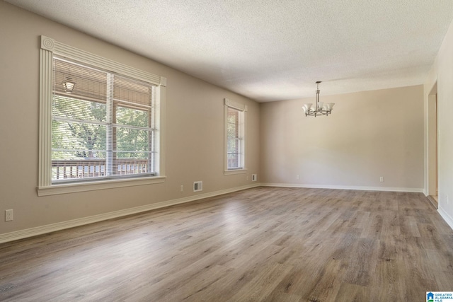 spare room featuring an inviting chandelier, baseboards, a textured ceiling, light wood finished floors, and visible vents