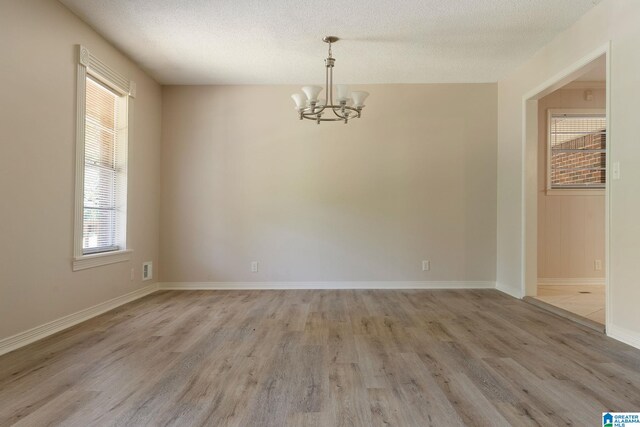 empty room with a chandelier, light hardwood / wood-style floors, and a textured ceiling