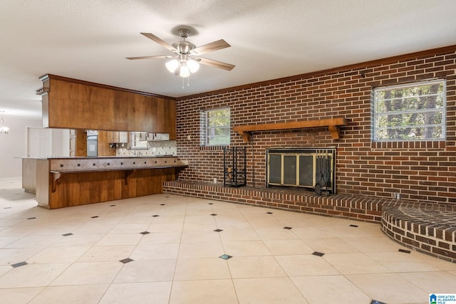 kitchen with a textured ceiling, a brick fireplace, tile patterned flooring, brick wall, and ceiling fan