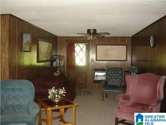 sitting room featuring ceiling fan, carpet flooring, heating unit, and wooden walls