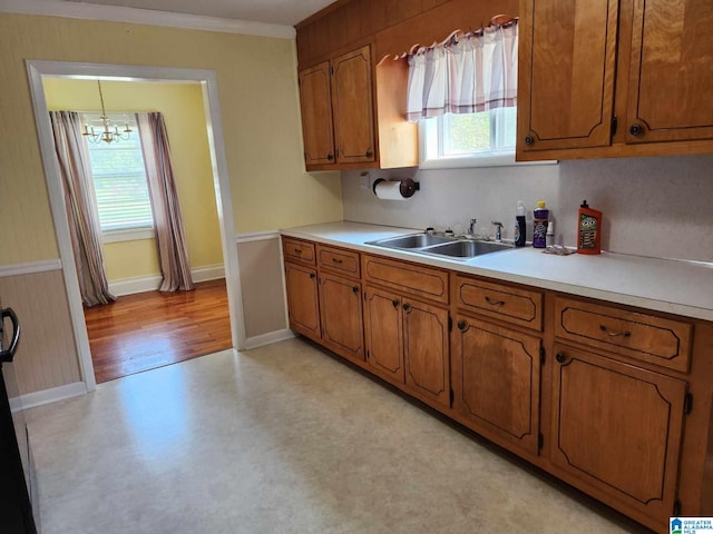 kitchen with hanging light fixtures, light wood-type flooring, ornamental molding, sink, and a chandelier