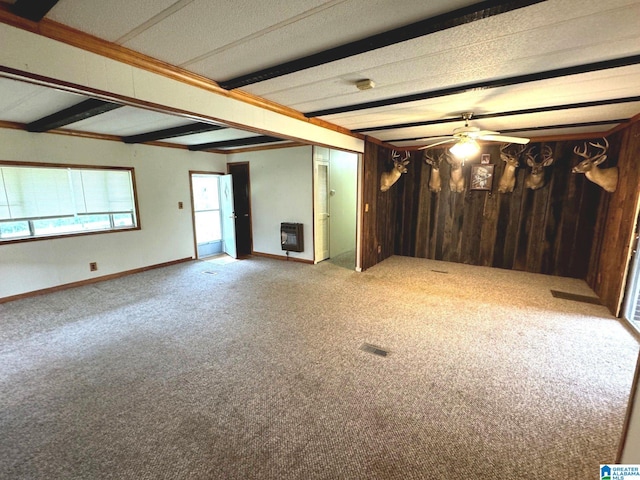 carpeted empty room featuring heating unit, beam ceiling, ceiling fan, and wooden walls