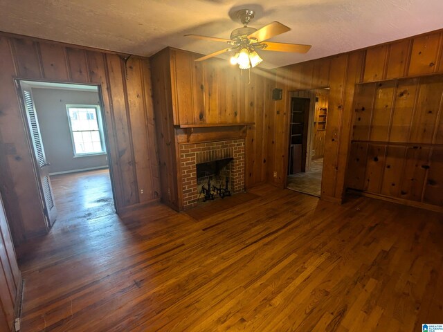 unfurnished living room with ceiling fan, a brick fireplace, a textured ceiling, wooden walls, and dark hardwood / wood-style flooring