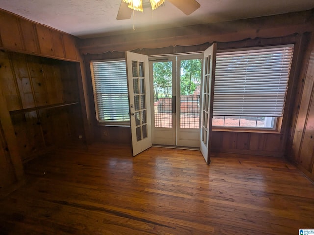 spare room featuring a healthy amount of sunlight, wooden walls, dark hardwood / wood-style flooring, and ceiling fan