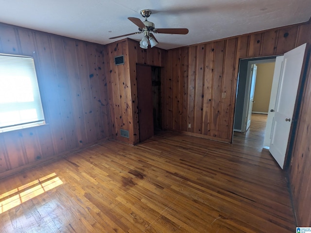 empty room with wooden walls, ceiling fan, and hardwood / wood-style floors