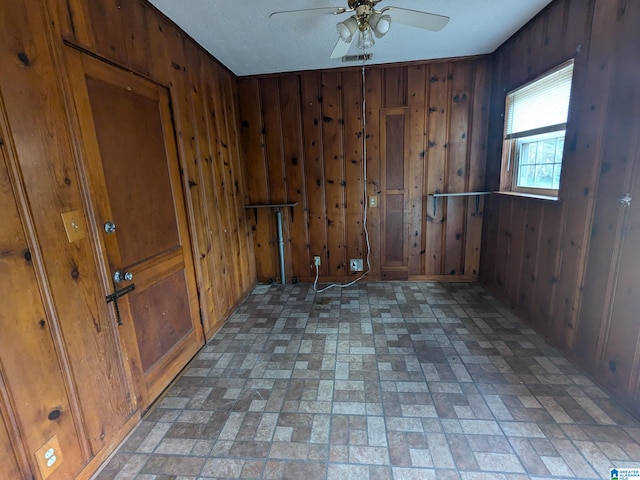 spare room with wood walls, ceiling fan, and a textured ceiling