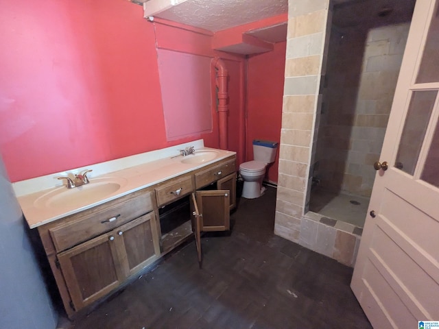 bathroom featuring wood-type flooring, a textured ceiling, tiled shower, vanity, and toilet