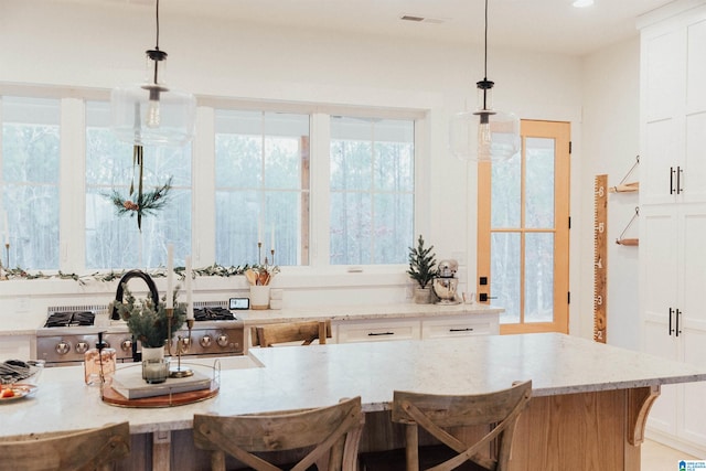 kitchen with a breakfast bar, white cabinetry, a healthy amount of sunlight, and decorative light fixtures