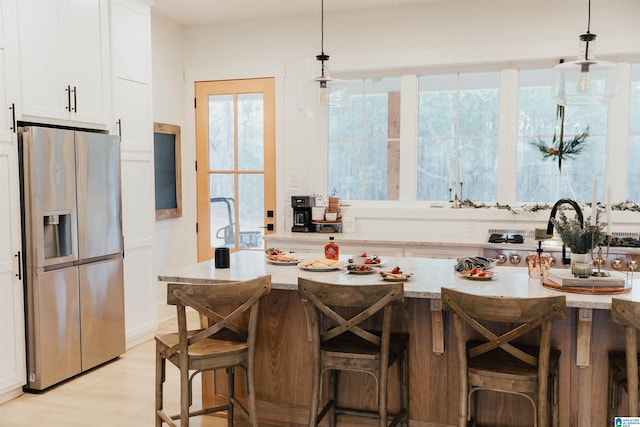 kitchen featuring hanging light fixtures, stainless steel fridge, white cabinets, and a breakfast bar