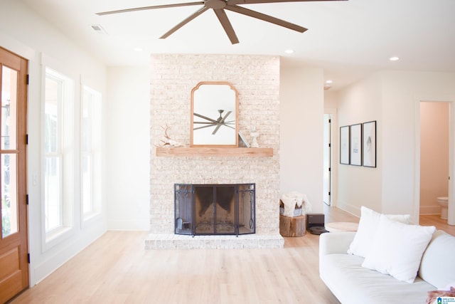 living room featuring a brick fireplace, ceiling fan, and light wood-type flooring