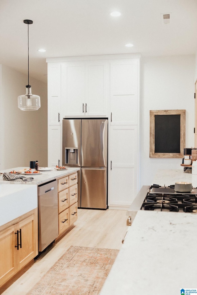 kitchen featuring appliances with stainless steel finishes, hanging light fixtures, light wood-type flooring, and light brown cabinetry