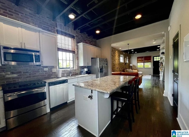 kitchen featuring brick wall, stainless steel appliances, dark hardwood / wood-style flooring, and a kitchen island