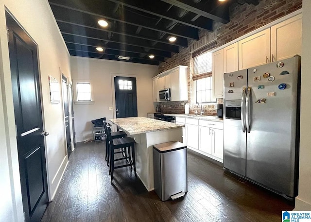 kitchen featuring brick wall, plenty of natural light, white cabinetry, appliances with stainless steel finishes, and a center island