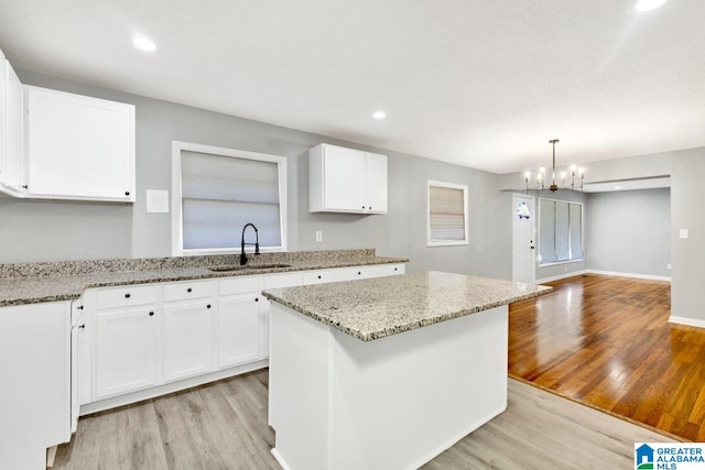 kitchen with white cabinets, sink, a center island, an inviting chandelier, and light wood-type flooring