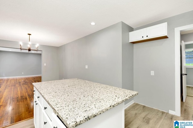 kitchen with light stone counters, white cabinets, a center island, light hardwood / wood-style flooring, and decorative light fixtures