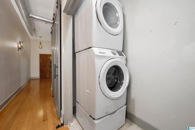 laundry area with light hardwood / wood-style floors and stacked washer and clothes dryer