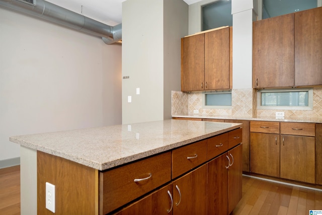 kitchen featuring light stone countertops, backsplash, light hardwood / wood-style flooring, and a kitchen island