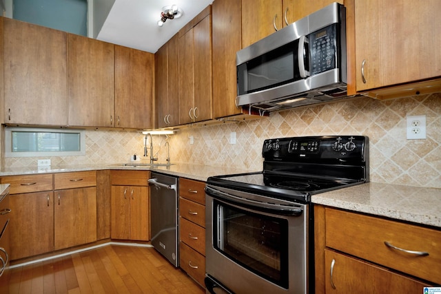 kitchen featuring sink, light stone countertops, light wood-type flooring, tasteful backsplash, and stainless steel appliances