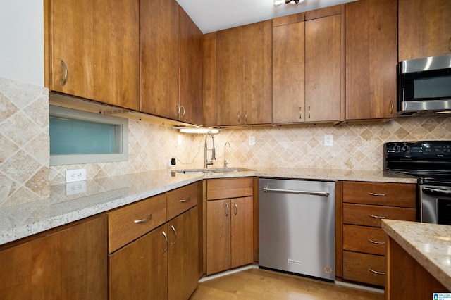 kitchen featuring appliances with stainless steel finishes, light wood-type flooring, tasteful backsplash, and light stone counters