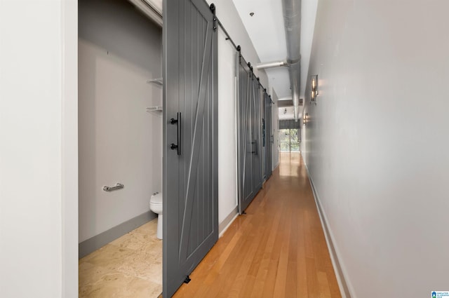 corridor with a barn door and wood-type flooring