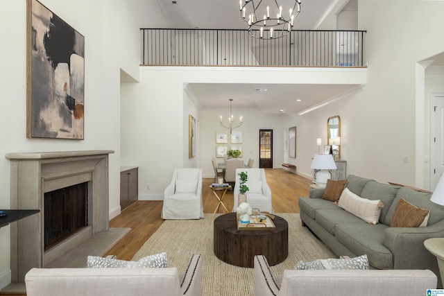 living room with a towering ceiling, a fireplace, an inviting chandelier, and wood finished floors