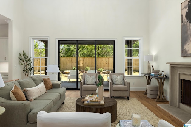 living room featuring a fireplace, a high ceiling, baseboards, and wood finished floors