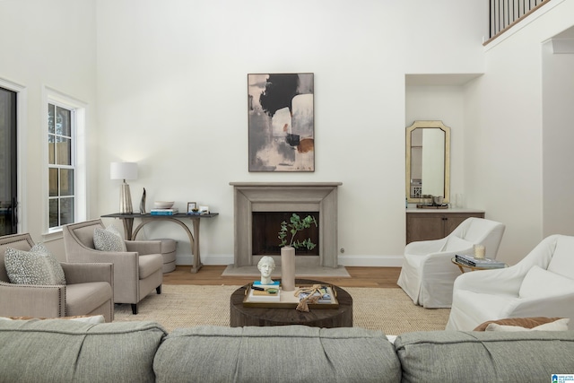 living room with a fireplace with raised hearth, baseboards, a towering ceiling, and wood finished floors