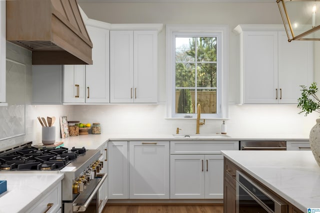 kitchen featuring high end range, beverage cooler, light stone countertops, a sink, and white cabinets